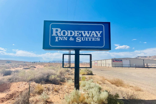 Sign for Rodeway Inn & Suites in a desert landscape with clear blue sky and nearby buildings in the background.