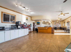 Spacious room with tiled floors, white cabinets, coffee machine, and a curved wooden counter. Ceiling fans and natural light enhance a dining area with tables and chairs in the background.