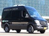 Black Mercedes-Benz Sprinter van with "American Dream" text on the side, parked in front of a glass building.