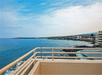 View from a balcony overlooking a vast body of water with a distant shoreline, showing buildings and greenery under a partly cloudy sky.