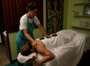 A person receives a hot stone massage from a therapist in a room with green walls and a vibrant wall hanging.