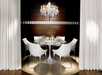 A round dining table with six white chairs is set for a meal under a modern chandelier, surrounded by white curtains and a dark accent wall.