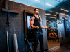 A man in athletic wear uses resistance bands attached to a wall-mounted fitness machine in a modern gym.