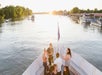 People gathered at the front of the boat chatting with drinks in hand at sunset on the Sacramento River: Alive After Five Cruise.