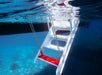 A white and red boat ladder is partially submerged in clear blue water, with underwater details visible below the surface.