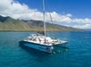A white catamaran anchored in clear blue water near green mountains, with several people swimming and relaxing on the boat under a sunny sky.