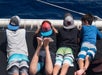 Four kids lying on a catamaran net enjoying the ocean views on a sunny day.