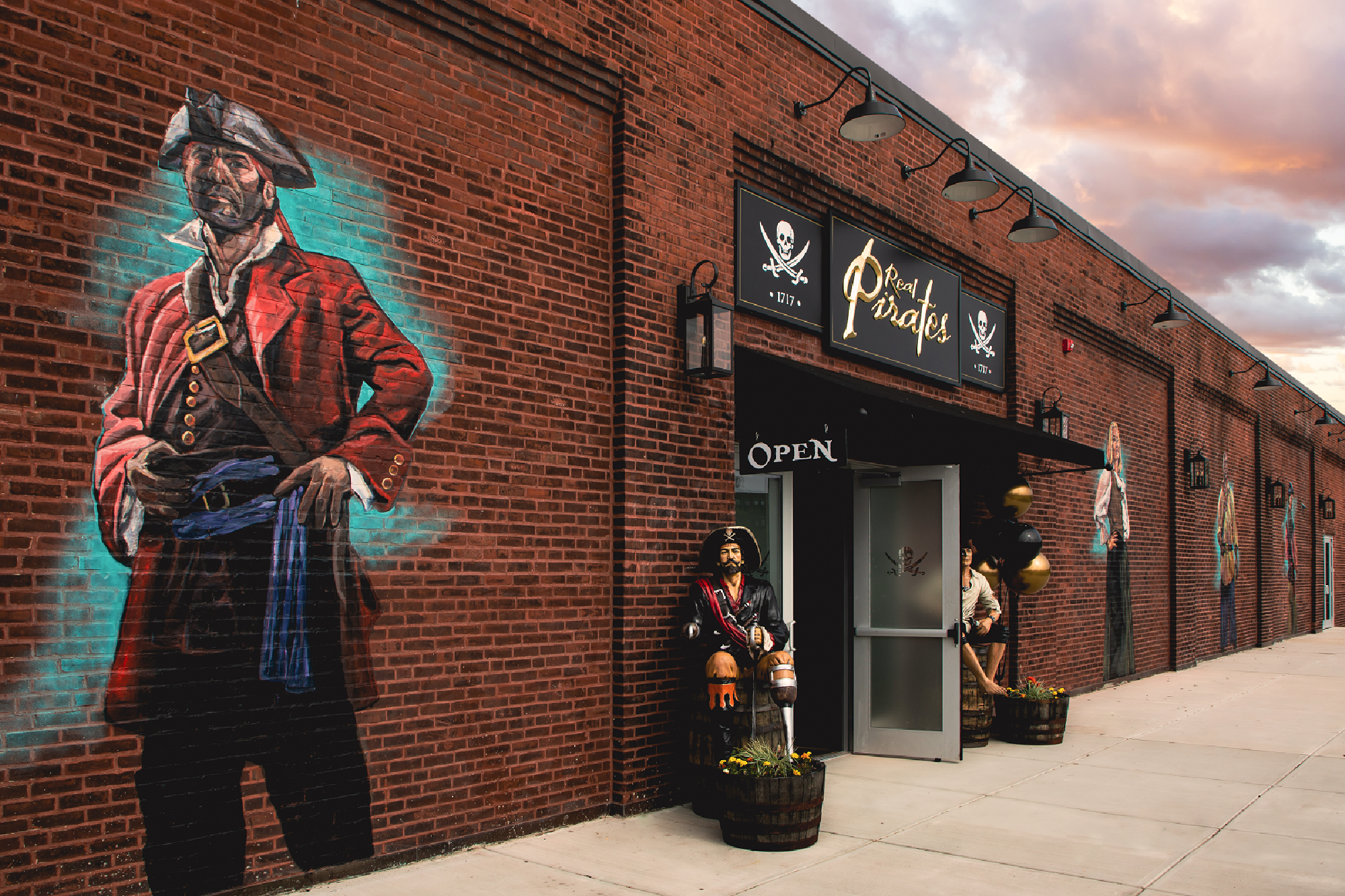 A brick building with pirate-themed murals and statues at the entrance, featuring a sign that reads "Pirate's" and an "open" sign by the door.