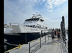 A white ferry named "Nathaniel Bowditch" is docked at a pier as people walk toward the boarding area under a partly cloudy sky.