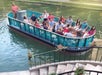 A group of people on a turquoise tour boat ride along a canal. The surroundings include a stone stairway and greenery, with flower pots by the water.