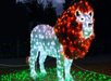 A lion sculpture made of white and orange lights stands on a grassy surface, illuminated against a dark sky.