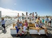 Several tourists onboard the San Diego Best of the Bay Harbor Cruise vessel, with some seated on benches while others standing just enjoying the beautiful views of the marina on a sunny day.