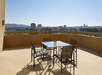 Rooftop patio with a glass table and four chairs overlooking a city skyline under a clear blue sky.