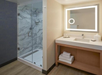 Modern bathroom with a glass-enclosed shower, marble-patterned tiles, a vanity with a large mirror, and neatly folded towels on a wooden shelf.