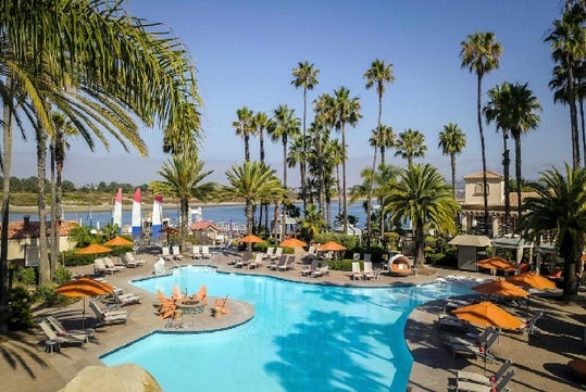 Outdoor swimming pool surrounded with trees, poolside chairs, and parasols.