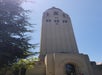 Tall beige tower with an arched entrance and a dome on top, surrounded by trees under a clear blue sky.