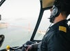 Helicopter pilot with headset flies over a body of water with the Golden Gate Bridge visible in the background.