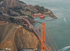 A red seaplane flies over the Golden Gate Bridge, with the bay and rugged coastline in the background.