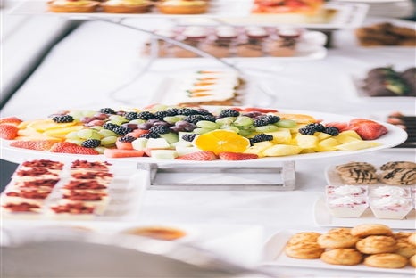 A large tray full of different fruits sitting on a table surrounded by different desserts on the San Francisco Lunch Cruise by Hornblower.