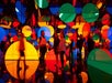 People walk through an art installation with large, colorful circular shapes and mirrors creating vibrant reflections and visual effects.