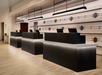 A modern hotel reception area with three sleek, black counters. The wall features a unique design with horizontal lines and circular elements. Lighting fixtures hang above the counters.