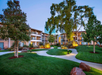 View of a landscaped courtyard with green lawns, trees, and shrubs, surrounded by multi-story residential buildings at dusk.