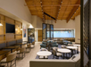Modern lounge area with wooden ceiling, round and rectangular tables, and upholstered chairs. Large screen on the wall and decorative partition in the center.
