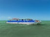 A blue and white tour boat with people onboard floats on calm green water under a clear blue sky.