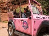 A bright pink jeep with "Pink Jeep Tours" branding carries four passengers and a driver through a rocky, desert landscape.