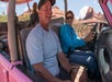 People riding in a pink open-air jeep through a rocky desert landscape, with two passengers and a driver smiling.