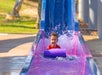 A young boy splashing into the water at the end of a purple water slide at Schlitterbahn New Braunfels in San Antonio, Texas.