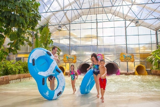 A family carrying blue tubes and laughing at Schlitterbahn New Braunfels in San Antonio, Texas.