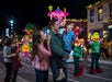 Family enjoying a nighttime parade with colorful floats and characters on a lively street.