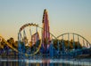 A view of the Wave Breaker roller coaster at SeaWorld San Antonio, featuring blue and yellow tracks over the water at sunset.