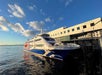 A blue and white passenger ferry is docked at the Port of Seattle terminal on a sunny day with scattered clouds.