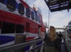 People walk up a gangway toward a large red, white, and blue passenger ferry docked at a terminal under a partly cloudy sky.