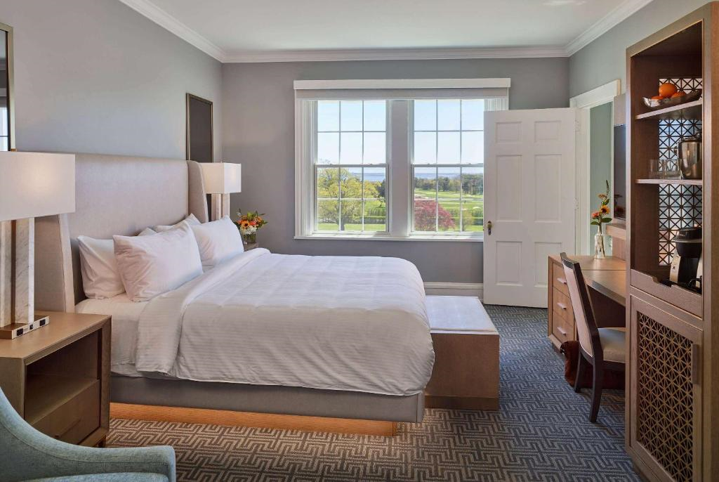 Hotel room with a large bed, bedside tables, a desk with a chair, and a window showing a view of a green landscape.