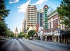 A downtown street scene with the Texas State Capitol in the background. Two theaters, Paramount and State, are visible along the street lined with trees and tall buildings.