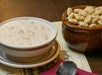 A bowl of creamy chowder next to a brown bowl of oyster crackers on a table with a spoon and red napkin.