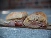 A close-up of a sandwich with cured meat, cheese, and a spread, sliced in half and placed on paper.