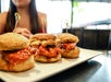 Three chicken biscuit sliders on a white plate, each held together with a toothpick; a person sits in the blurred background.