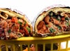 Two halves of a burrito with meat, beans, and greens wrapped in foil, placed in a yellow basket.