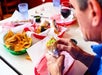 A person holds a wrapped burrito at a table with baskets of tortilla chips and drinks in a casual dining setting.