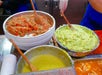 Bowls of fresh salsa, guacamole, and green sauce with wooden spoons are arranged on a countertop, ready for serving.