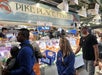 People shopping at Pike Place Fish Co, with staff in orange aprons serving customers from behind the seafood counter.