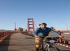 A person wearing a helmet rides a bicycle on the Golden Gate Bridge in San Francisco under a clear blue sky.