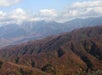Mountain range under a partly cloudy sky with rolling hills covered in autumn foliage in the foreground.