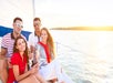 Four people sit on a sailboat holding glasses and smiling, with water and sunlight in the background.