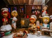 Four life-sized elf puppets in a festive kitchen scene, wearing chef hats and aprons, surrounded by baking supplies and holiday decorations.