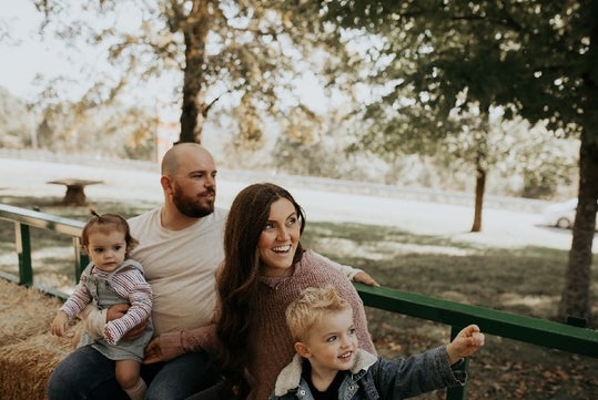 A family of four with two young kids laughing and having white on a hayride on a fall day at Shepherd’s Pumpkin Fest.